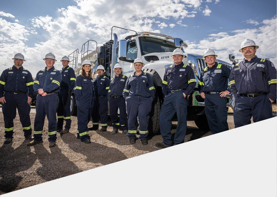 pictured: ten EnviroServe employees wearing jumpsuits and hard hats stand in front of a large truck