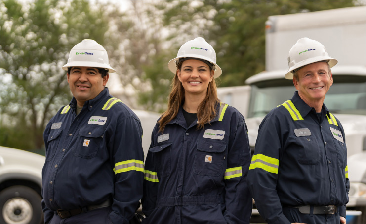 pictured: three EnviroServe workers wearing safety coveralls and hardhats smile