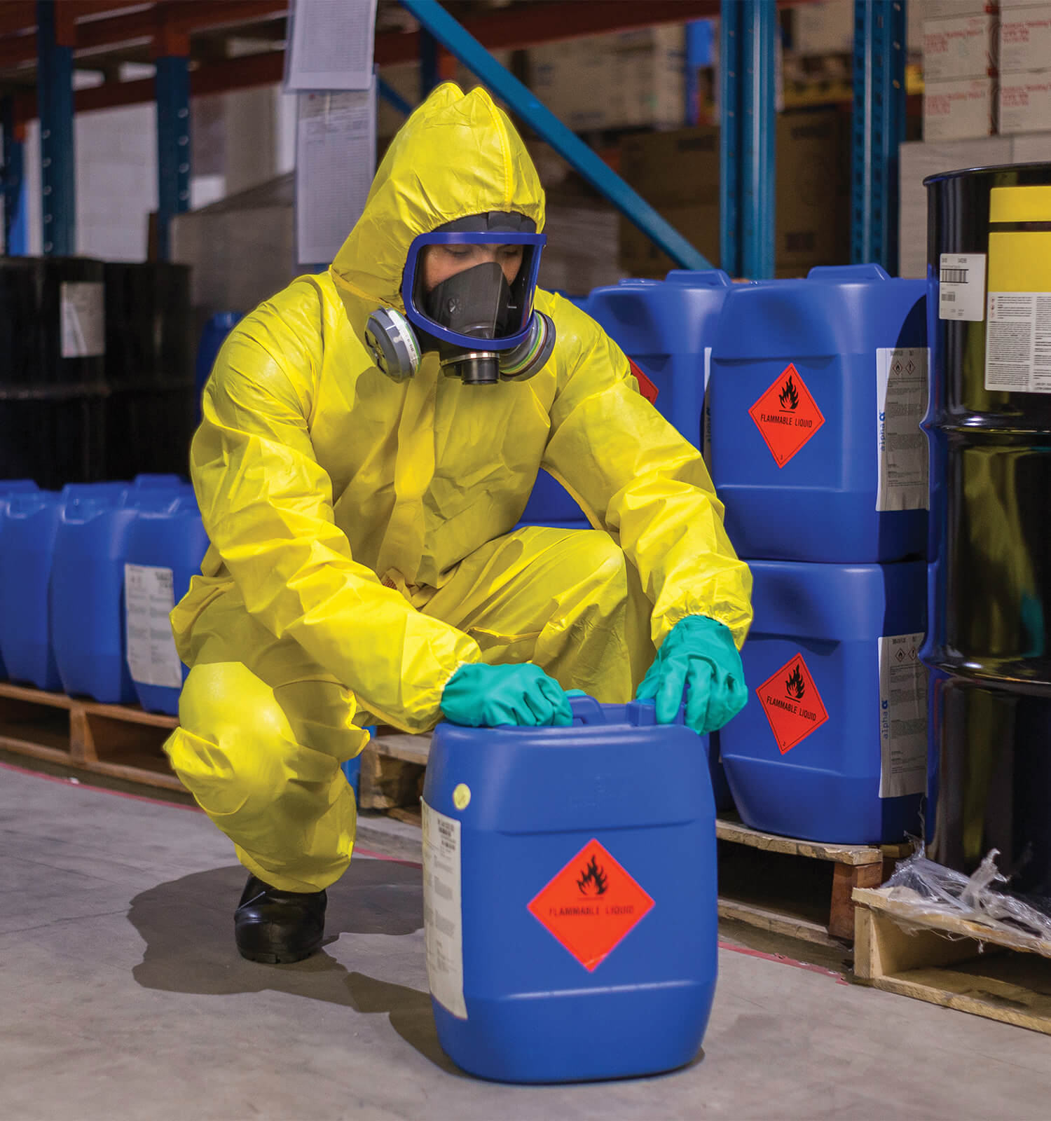 pictured: an EnviroServe worker wearing a yellow hazmat suit and gas mask closes a blue jug marked FLAMMABLE