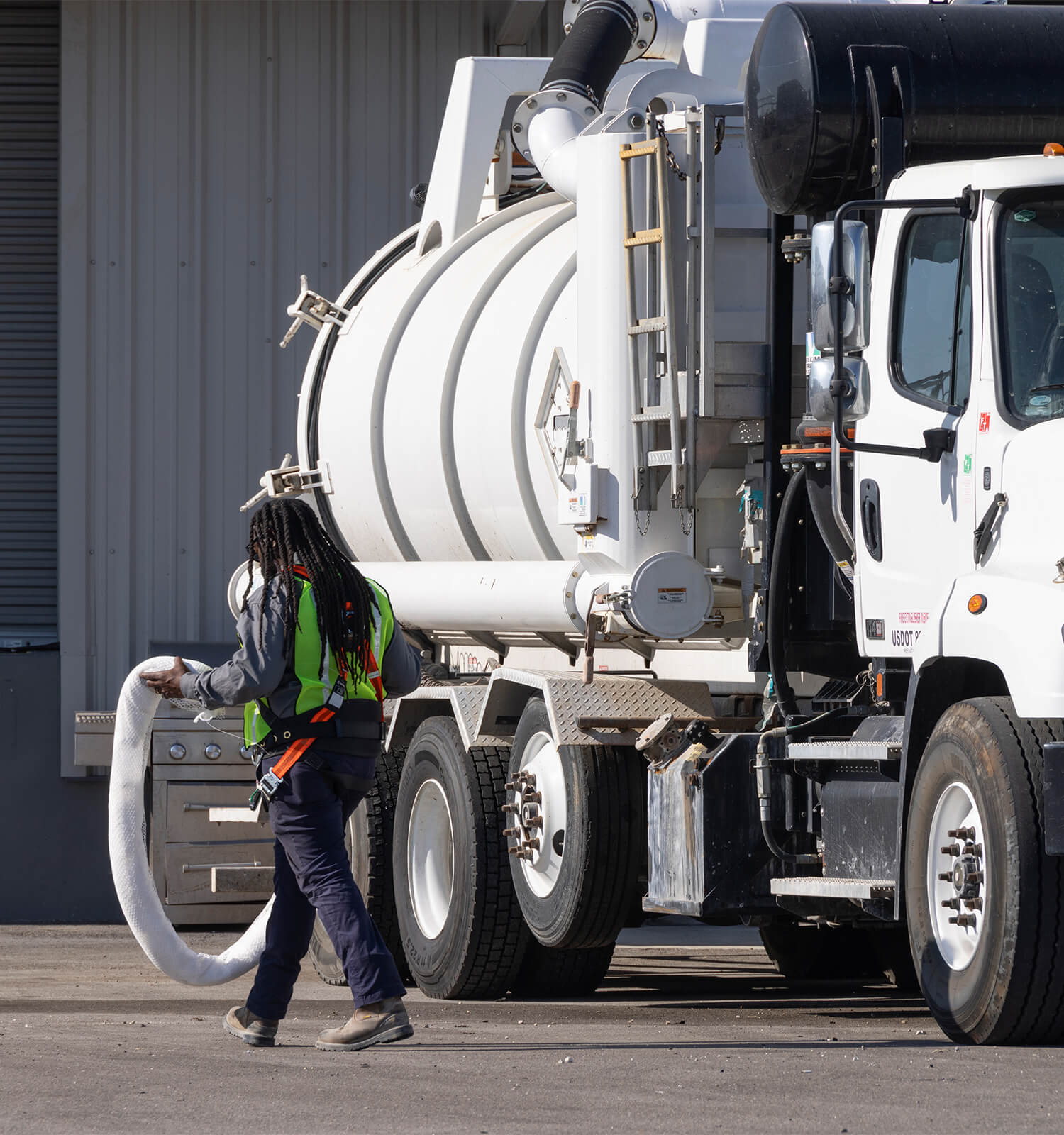 pictured: an EnviroServe worker carries a large hose next to a pump truck