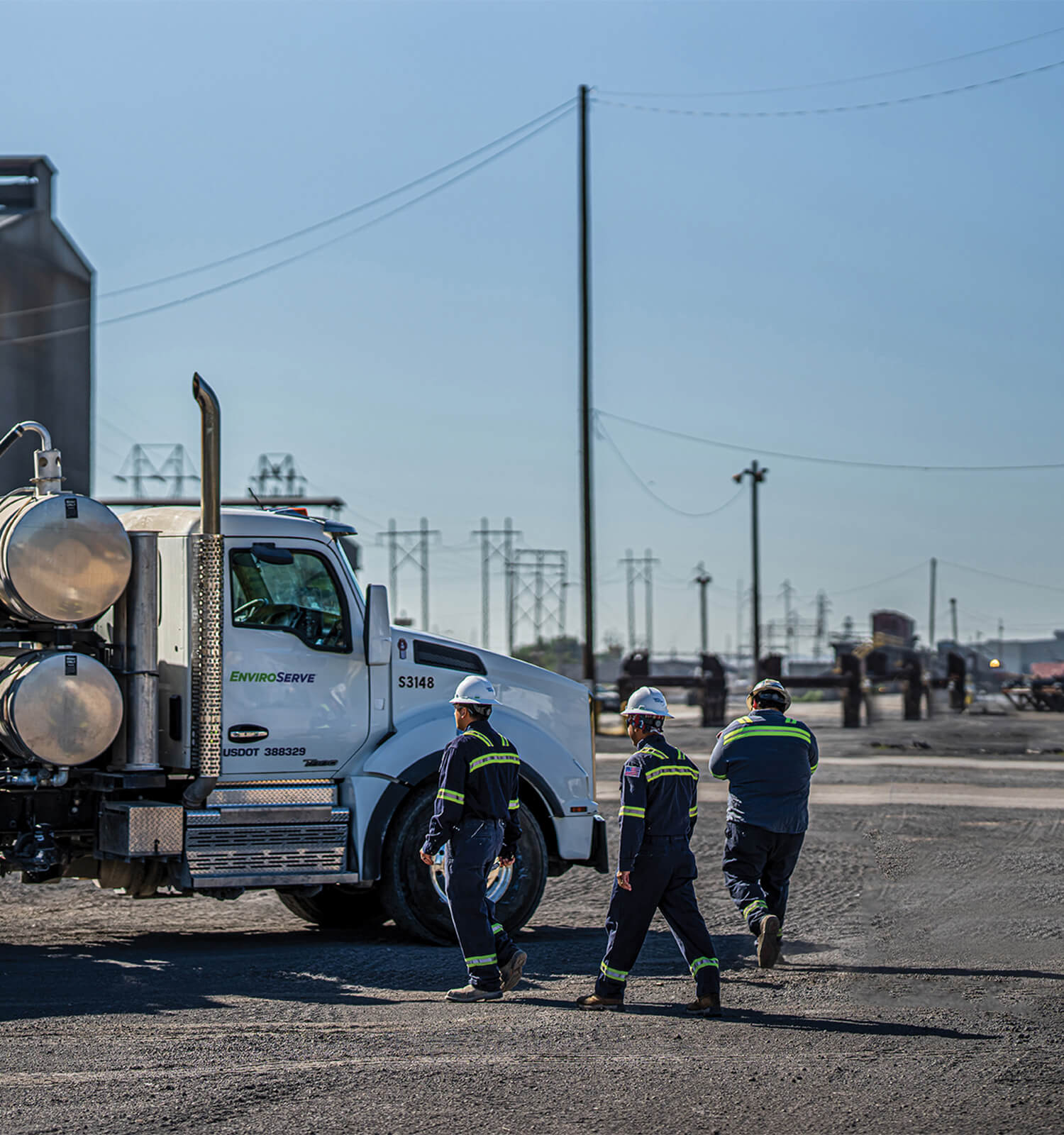 pictured: three EnviroServe workers walking beside a white semi truck